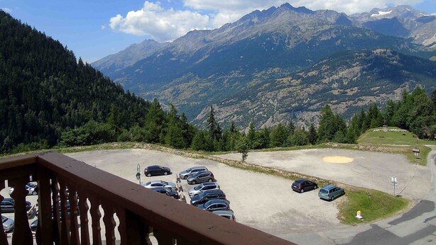 A parking area with cars, a mountain view, and a forested hillside.