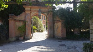 An arched stone gateway with a lantern, surrounded by greenery and a gravel path leading to a building.