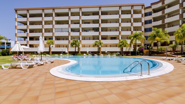 Un hotel con una piscina grande, varios balcones y palmeras.