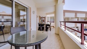 Un balcón con mesa y sillas de vidrio, un comedor con mesa y sillas, y vistas de los edificios circundantes.