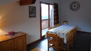 Un coin repas avec une table dressée pour quatre personnes, des chaises en bois, une horloge au mur et une fenêtre avec des rideaux.