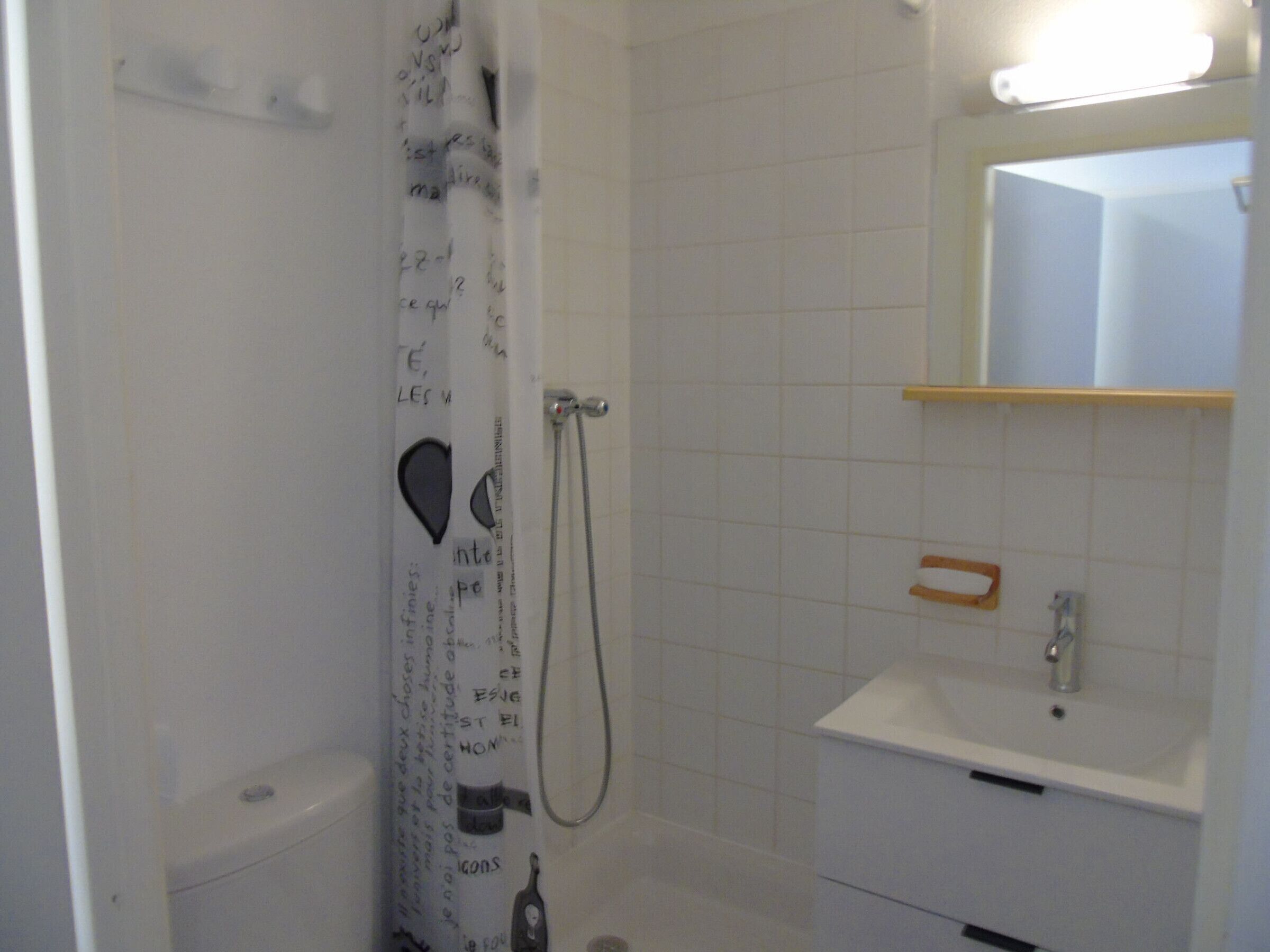 A small bathroom with a shower, toilet, sink, and mirror.