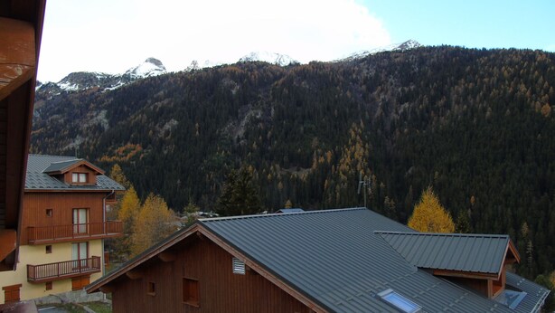 Un chalet en bois doté d’un toit en pente, d’un balcon et offrant une vue sur une chaîne de montagnes boisées.