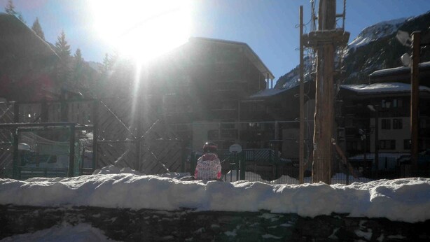 A snowy outdoor area with a stone wall and a metal fence.