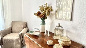 Una sala de estar acogedora con una mesa de centro de madera, un sillón color beige, un jarrón con flores secas, un candelabro y una jaula decorativa.