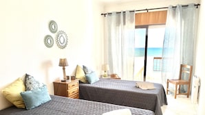 Habitación de hotel con dos camas, un aparador de madera, una silla y vista al mar por la ventana.