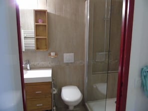 Un bagno con il water, un lavandino, un box doccia e una mensola in legno con un oggetto rosa.