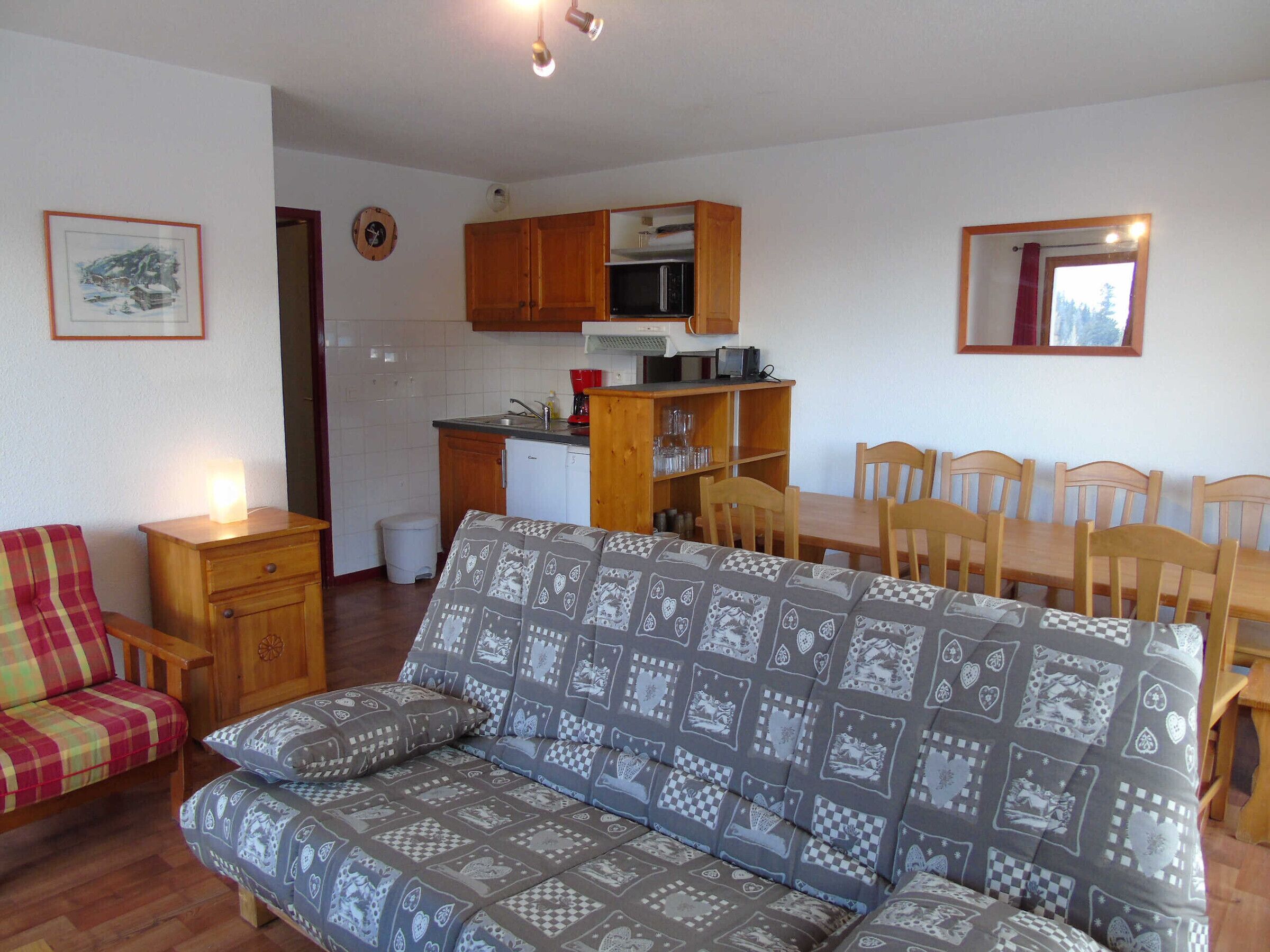 Uma sala de estar aconchegante com um sofá estampado, uma mesa de jantar de madeira com cadeiras e uma cozinha com armários de madeira e uma geladeira.