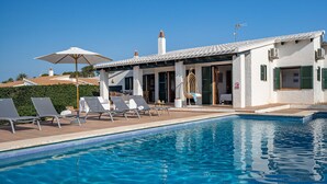 Ein Poolbereich mit Liegestühlen, einer überdachten Lounge und einem Gebäude mit einem Ziegeldach.