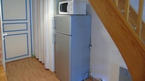 Eine kleine Küche mit einer Mikrowelle auf dem Kühlschrank, einer Holztreppe und einer Tür mit blauen Verzierungen.