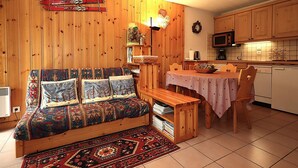A cozy room with a wooden sofa, a dining table, and a kitchen area with wooden cabinets and a microwave. - 2-room cabin apartment in Les Houches, balcony, sleeps 4 (Les Houches)
