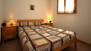 A neatly made bed with a patterned bedspread, two bedside lamps, a small bedside table with a lamp, a picture frame on the wall, and a window with curtains. - 2-room cabin apartment in Les Houches, balcony, sleeps 4 (Les Houches)