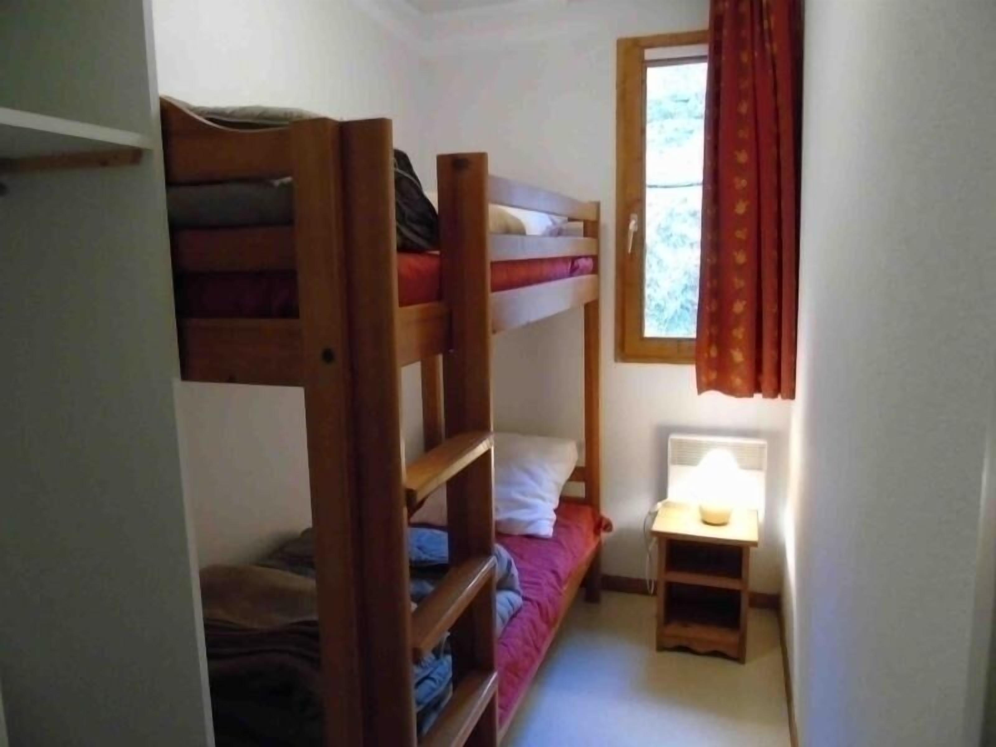 Une petite pièce, de taille modeste, avec des lits superposés, une petite table avec une lampe et une fenêtre avec des rideaux.