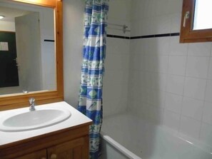 Ein Badezimmer mit einem Holzausleger, einem weißen Waschbecken, einem Spiegel und einer Dusche mit einem blau-weißen Vorhang.