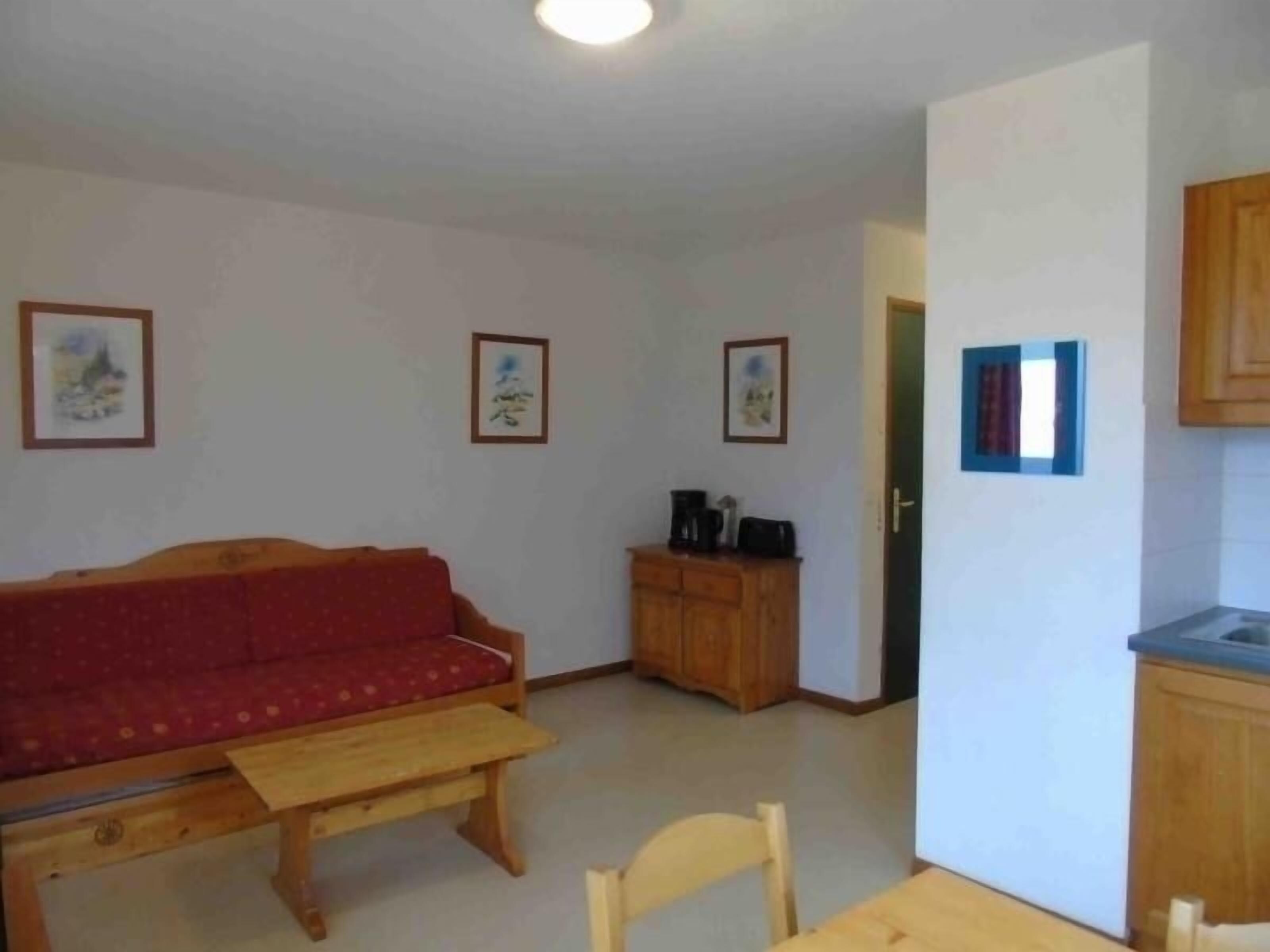 Una habitación pequeña y acogedora con un banco de madera, un sofá rojo, un armario de madera y una zona de kitchenette.