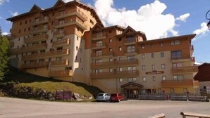 A multi-story hotel with balconies, a parking area, and a sign indicating a restaurant. - Valfréjus: 2-room apartment, near ski lift, pet-friendly (Valfréjus)