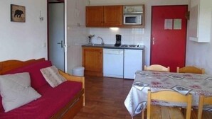 A compact room with a kitchenette, a dining table with chairs, a red door, and a bed with pillows. - Valfréjus: 2-room apartment, near ski lift, pet-friendly (Valfréjus)