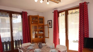 Un coin repas avec une table dressée pour quatre personnes, un buffet en bois contenant de la vaisselle et un téléviseur posé sur un meuble.