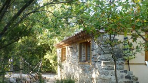 A stone building with a small window and a tiled roof, surrounded by trees and a gravel path. - La Petite Bergerie - pure nature! Vacation home in unspoiled nature. (Termes)