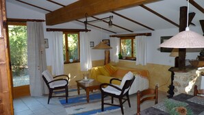 A cozy living room with a sofa, wooden chairs, a table, and a hanging lamp. - La Petite Bergerie - pure nature! Vacation home in unspoiled nature. (Termes)