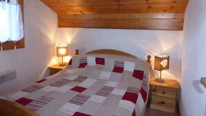 Une chambre à coucher avec un plafond en bois, un lit recouvert d’une courtepointe, deux tables de chevet avec des lampes et une fenêtre avec des rideaux.