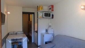 Et kompakt værelse med tekøkken, spiseplads og sofa.