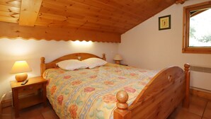 A wooden bed with a floral bedspread, wooden headboard, and nightstands with lamps. - 4-room apartment, pool and parking, near lifts (Les Houches)