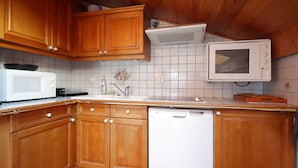 A compact kitchen with wooden cabinets, a white microwave, a built-in oven, and a dishwasher.
