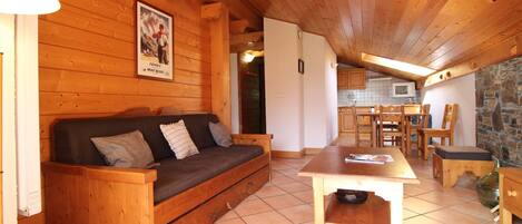 A cozy wooden cabin interior with a sofa, a dining table, and a kitchen area.
