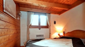 A cozy room with wooden walls, a bed with a quilt, a window with curtains, and a wall-mounted heater.