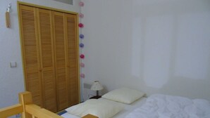 A bedroom with a wooden bed, white bedding, a wooden wardrobe, and a wall-mounted lamp. - Cozy 2-Room Mezzanine Apartment for 4, Steps from Lift & Shops in Valfréjus (Valfréjus)