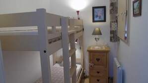 A bunk bed room with a bedside table, a lamp, and a dresser with heart-shaped handles.