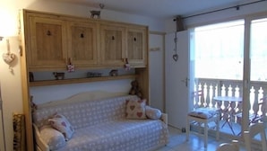 A cozy room with a sofa, wooden cabinets, a small table, and a balcony with chairs.