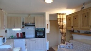 A compact kitchen with a microwave, toaster, and oven. There is a dining table with a patterned tablecloth. A sofa with heart-patterned cushions is in the living area.