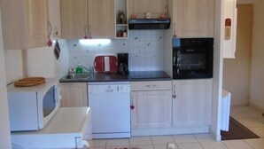 A compact kitchen with light wooden cabinets, a microwave, a dishwasher, a stove, and a sink.