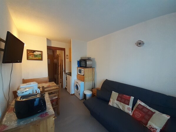 A compact living space with a sofa, a small table with a toaster, a microwave, and a washing machine. - Cozy studio in Valfréjus, near ski lifts (Valfréjus)