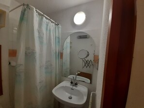 A bathroom with a shower curtain, a sink, a mirror, and a light fixture. - Cozy studio in Valfréjus, near ski lifts (Valfréjus)