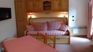 Une pièce confortable avec un lit, une armoire en bois au-dessus et une table recouverte d’une nappe rose.