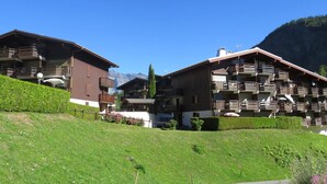 A chalet-style building with balconies, a clear sky, and a mountainous backdrop.
