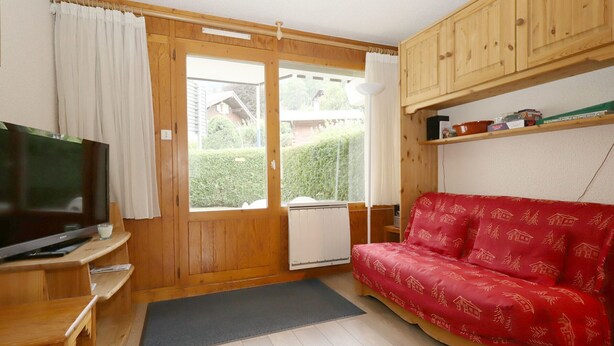A cozy room with a wooden TV stand, a red sofa, and a large window with curtains.