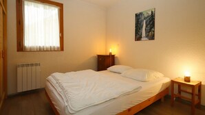 A bedroom with a wooden bed, a radiator, a window with curtains, a nightstand with a lamp, and a painting on the wall.