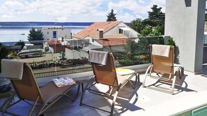 A balcony with two lounge chairs, a small table, and a view of a lake and buildings.