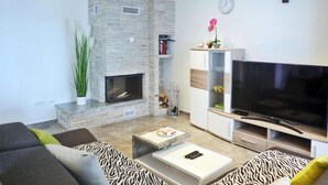 A modern living room with a stone fireplace, a flat-screen TV, and a sofa with zebra-patterned cushions.