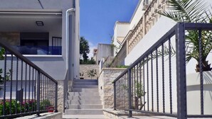 A modern building with a staircase leading to a balcony, surrounded by stone walls and metal railings.
