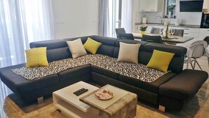 A modern living room with a sectional sofa, a coffee table, and a dining area with a kitchen in the background.
