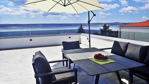 Eine Dachterrasse mit Tisch und Stühlen, einem großen Sonnenschirm und Blick auf das Meer.