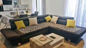 Ein modernes Wohnzimmer mit einer Eckcouch, einem Essbereich und einer Küche im Hintergrund.