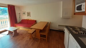A compact kitchen with a dining table, a red sofa, and a microwave. - Cozy 2-Room Apartment - Ski-In/Ski-Out, Balcony, Pet-Friendly, Sleeps 6 (Valfréjus)