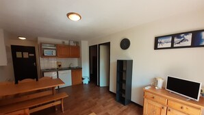 A compact living space with a kitchenette, a dining area, a TV, and a clock on the wall. - Cozy 2-Room Apartment - Ski-In/Ski-Out, Balcony, Pet-Friendly, Sleeps 6 (Valfréjus)