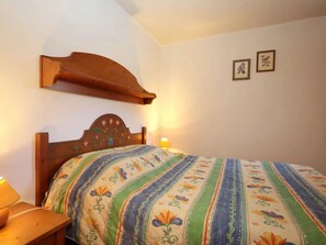 A bedroom with a wooden headboard, a floral-patterned bedspread, a bedside lamp, and two framed pictures on the wall. - 2-room cabin apartment, pool, pets allowed, near cable cars (Les Houches)